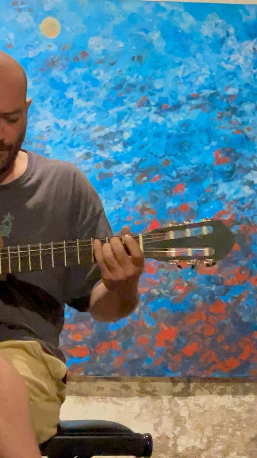 Ghaith Al Jammal playing guitar in front of a blue painting
